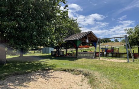 Bild sonniger Außen-Spielbereich Kita Höchstenbach mit Wiese, blauem Himmel und Schaukel
