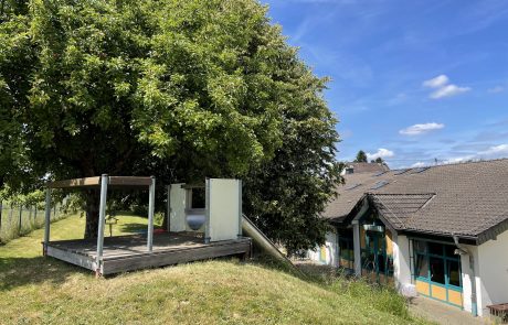 Bild sonniger Außen-Spielbereich Kita Höchstenbach mit Wiese und blauem Himmel